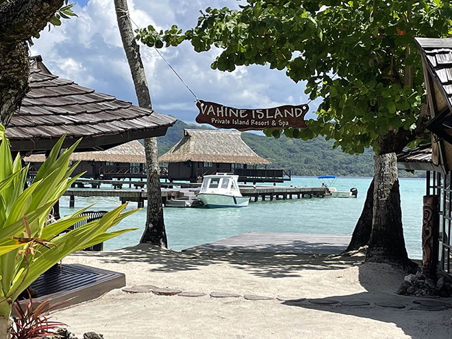 Vahine Private Island Resort & Spa sign looking out onto a blue bay with overwater huts and boats in French Polynesia.