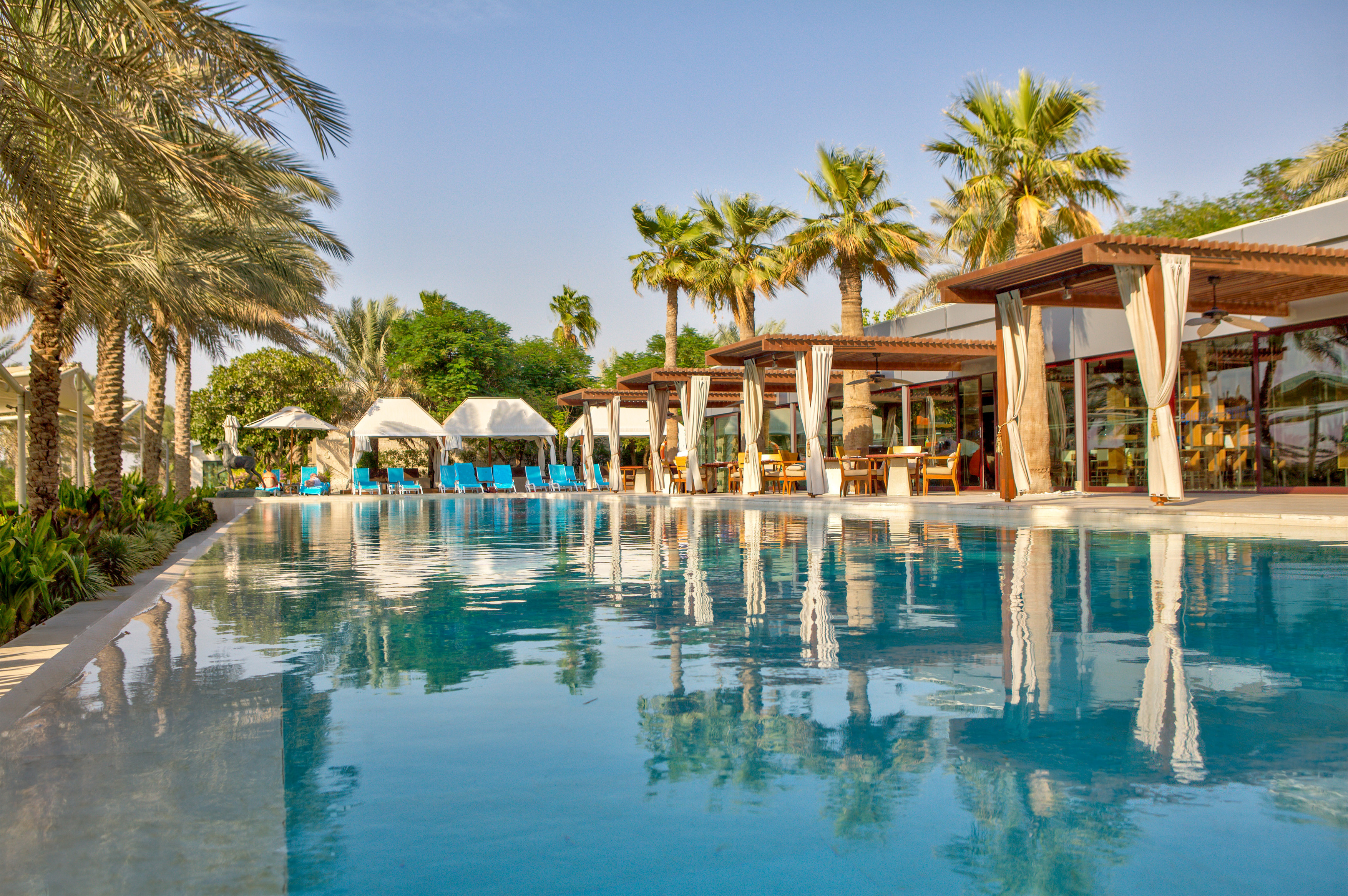 Sunlight shimmers on the swimming pool beneath palm-lined cloisters at Melia Desert Palm, Dubai