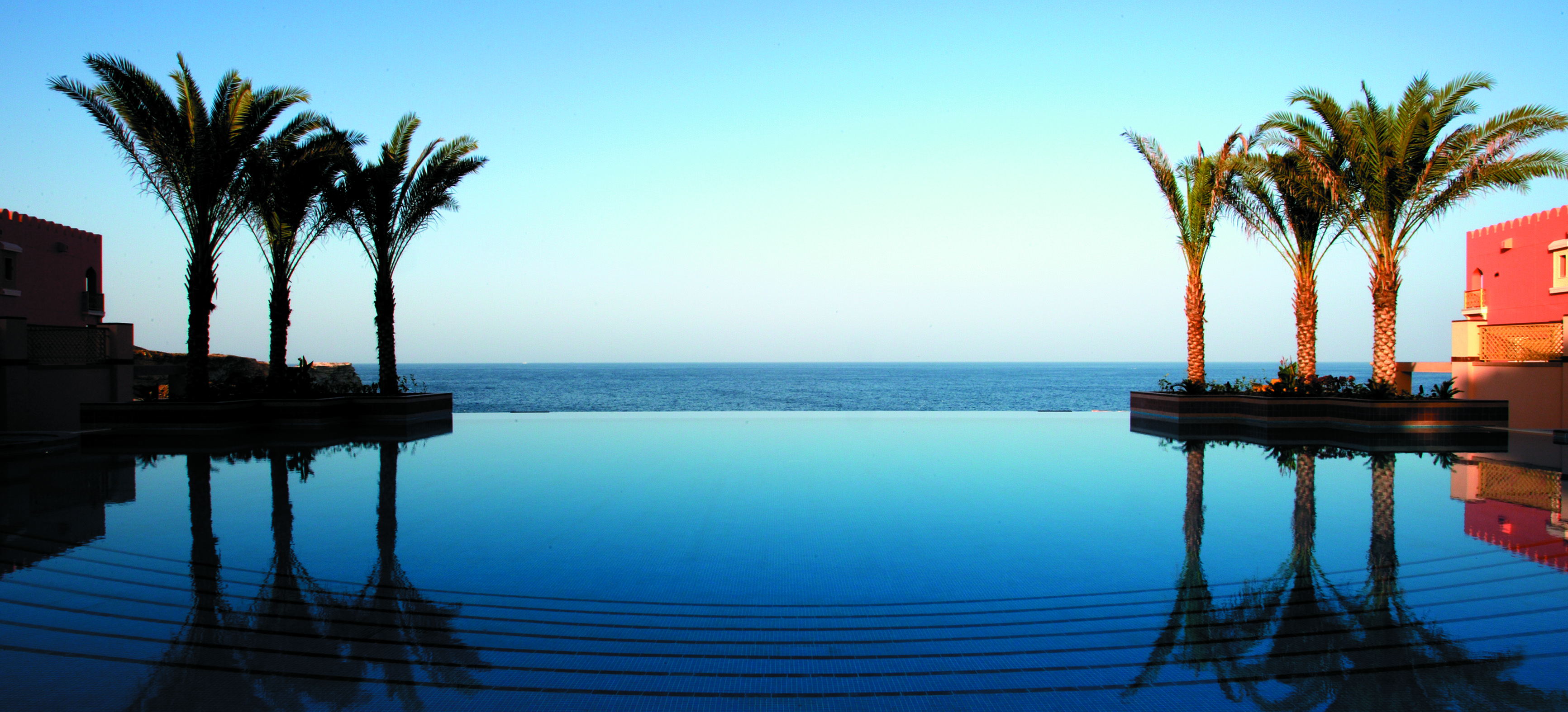 The infinity pool at sunrise over the Arabian gulf is mirror-like at Shangri-La al Husn Resort and Spa, Muscat, Oman