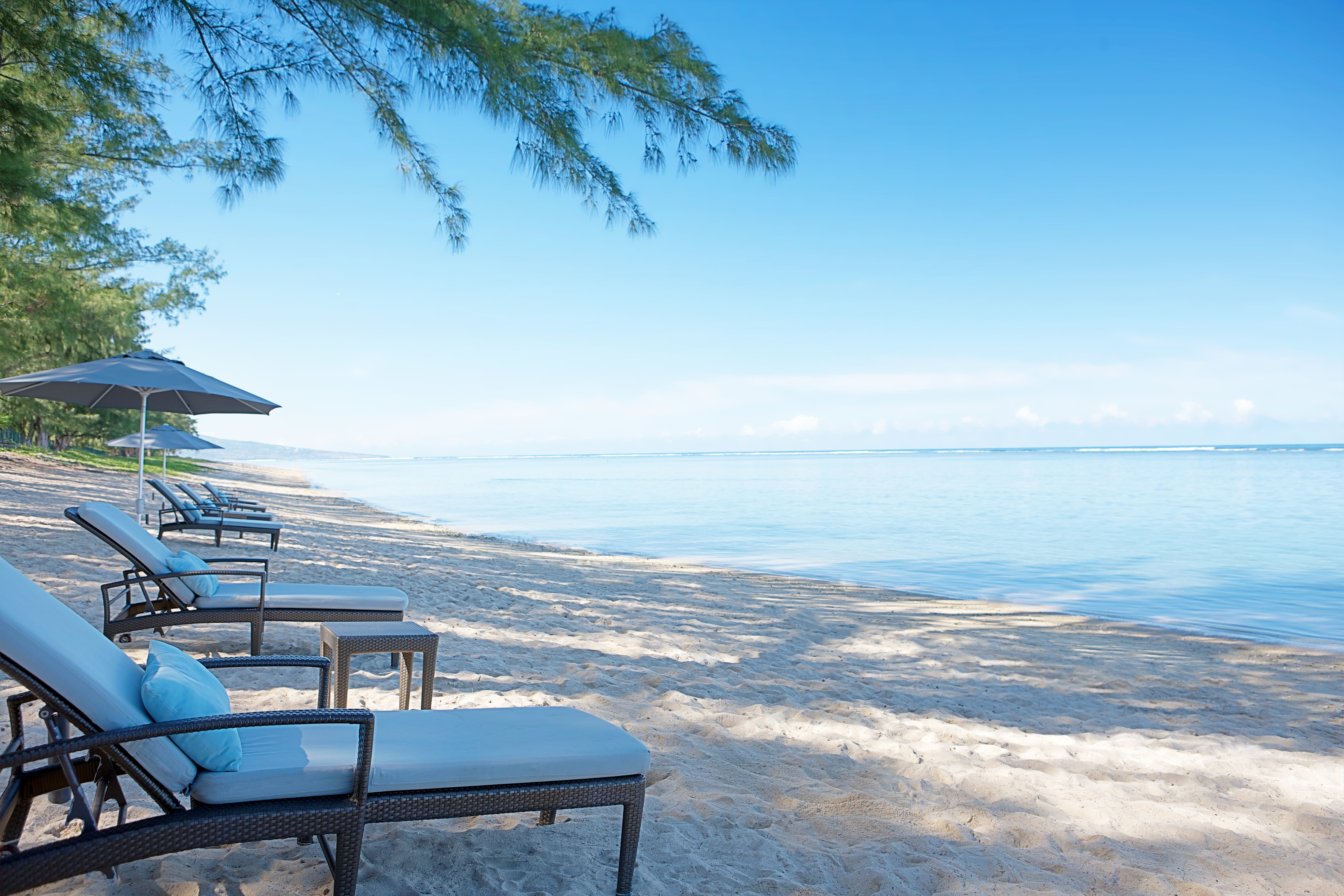 Shady sunloungers look out over the pristine white beach and blue sea at LUX* Saint Gilles Reunion