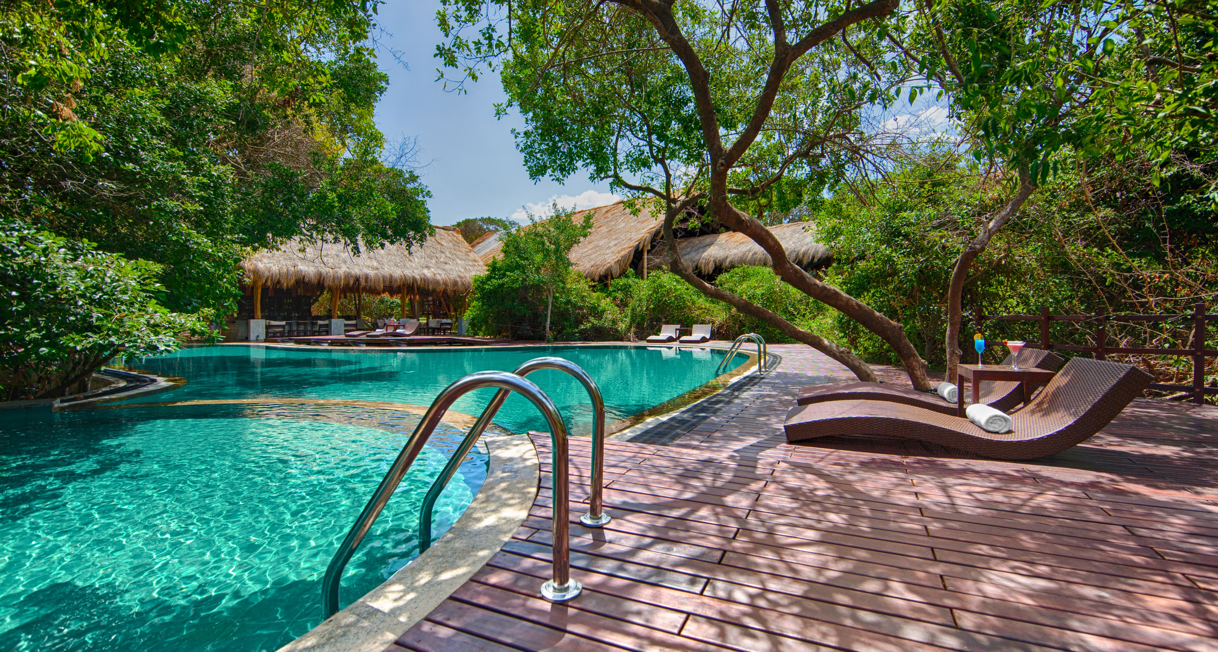 A sparkling turquoise pool stretches over to the traditional thatched roof of the main hotel building at Jungle Beach, Sri Lanka