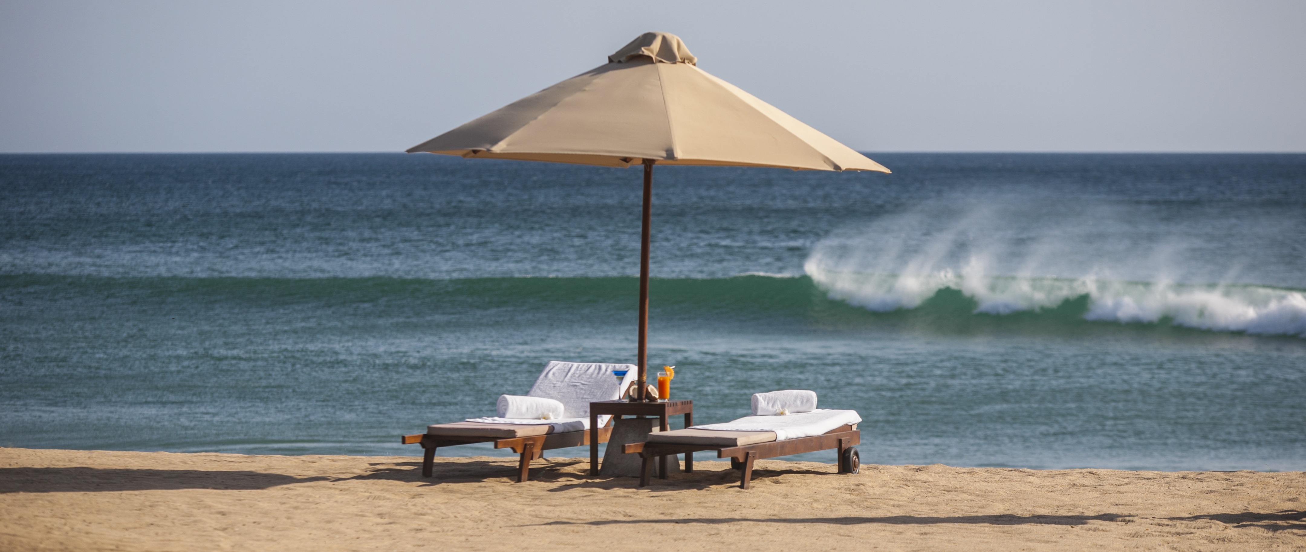 Two loungers sit beneath the shade of a parasol looking over an aquamarine sea at Jungle Beach, Sri Lanka