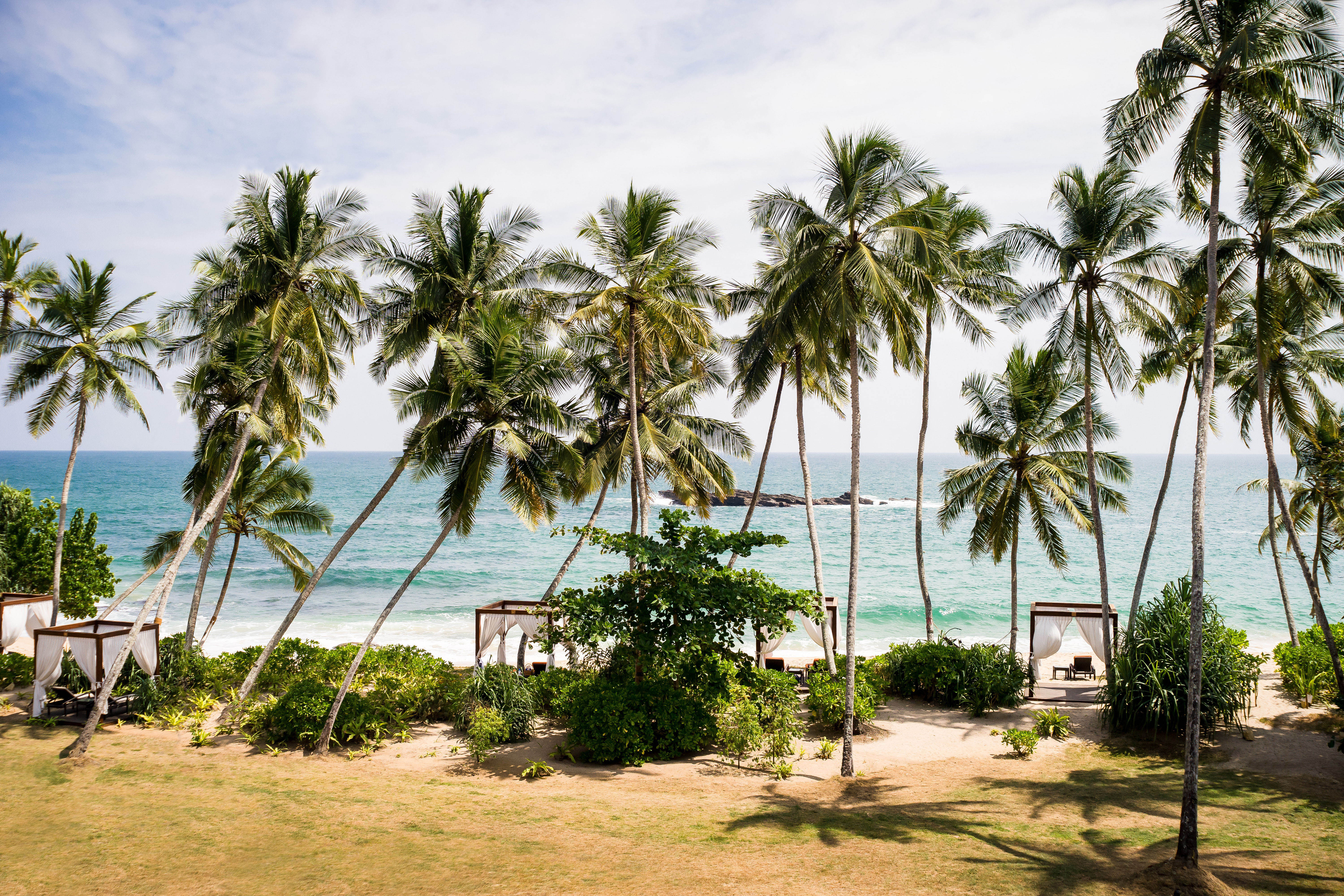 Beach cabanas sit beneath towering palms at the beach of Anantara Peace Haven, Tangalle, Sri Lanka