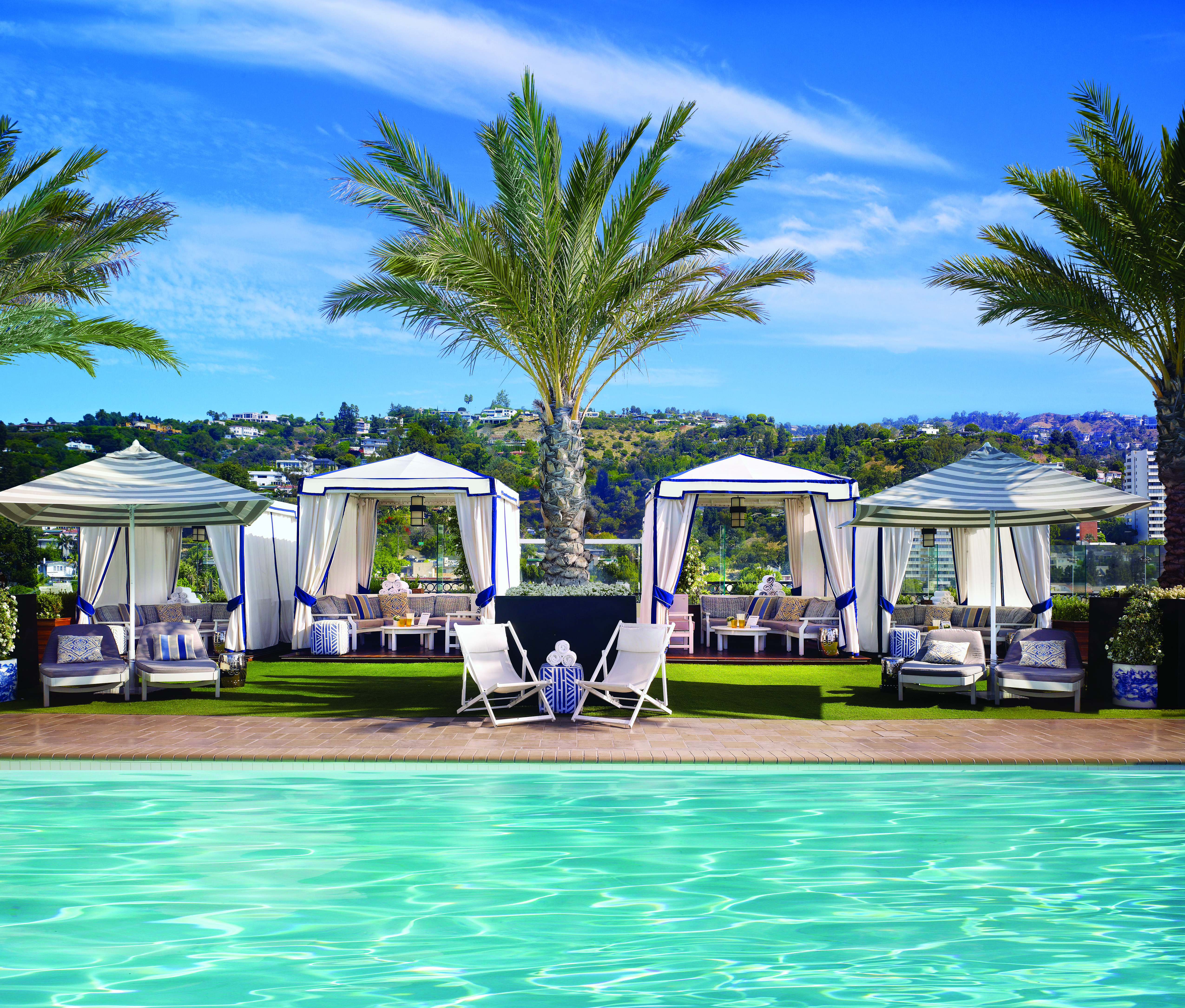 The brilliant turquoise waters of the rooftop pool lie in the front of billowing cabanas, towering palms and the the rolling LA vista at The London West Hollywood, USA