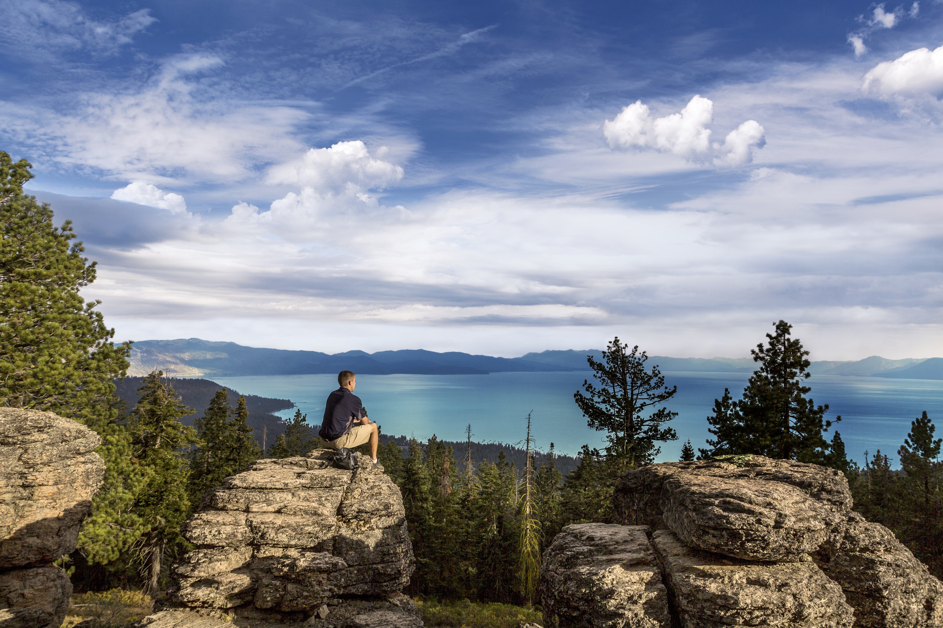 A hiker sits on a rock and surveys the view over the enormous, spectacular Lake Tahoe at The Ritz-Carlton Lake Tahoe, USA