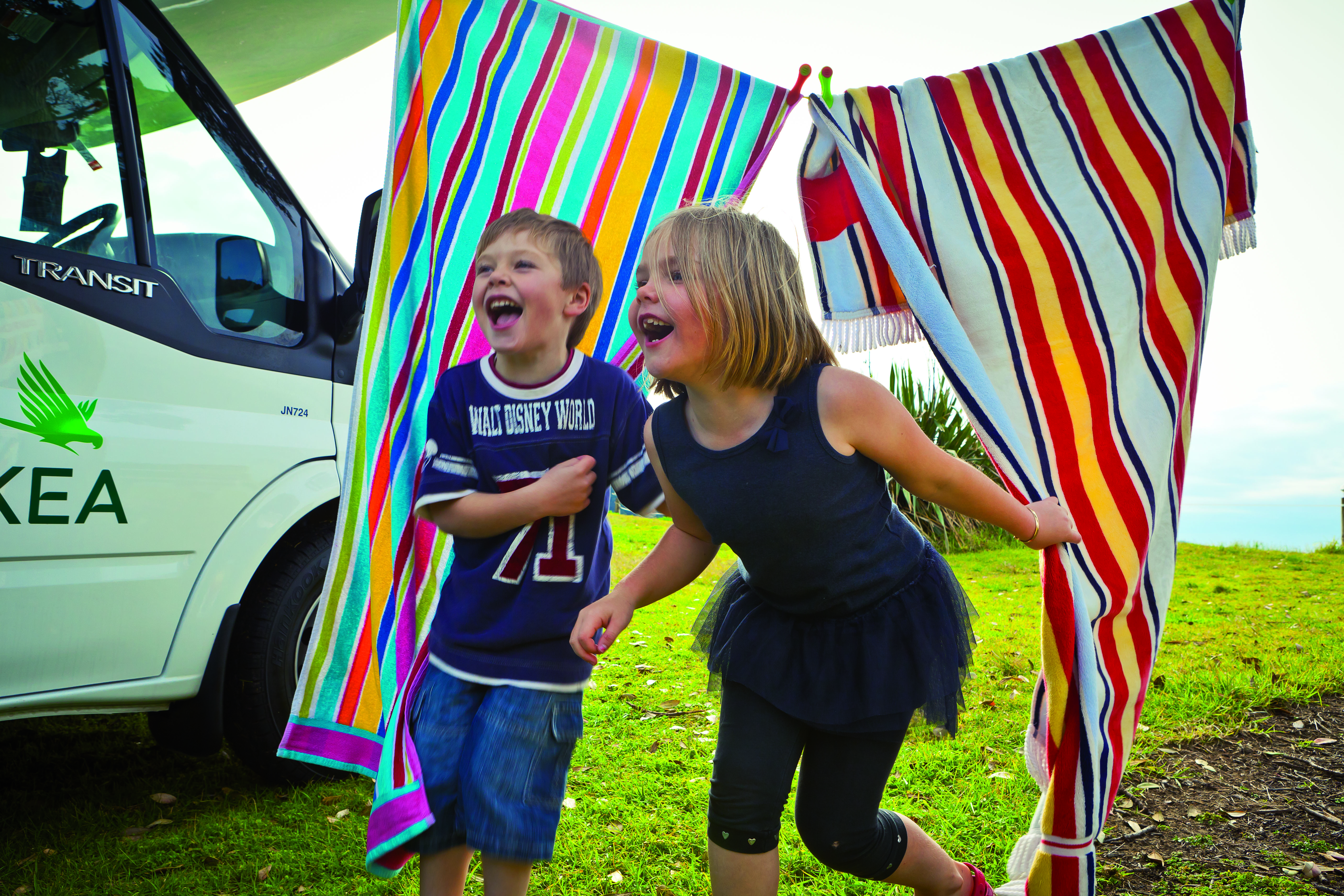 Children playing and laughing in towels on line next to campervan